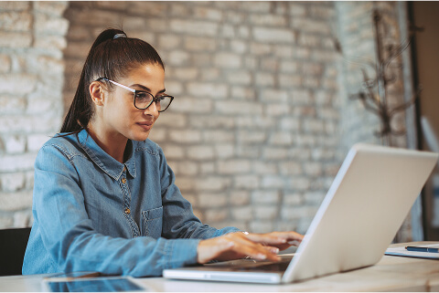 A young woman with a high ponytail and glasses is browsing Usenet on her laptop through Newshosting. She is smiling at something she’s reading in a newsgroup.