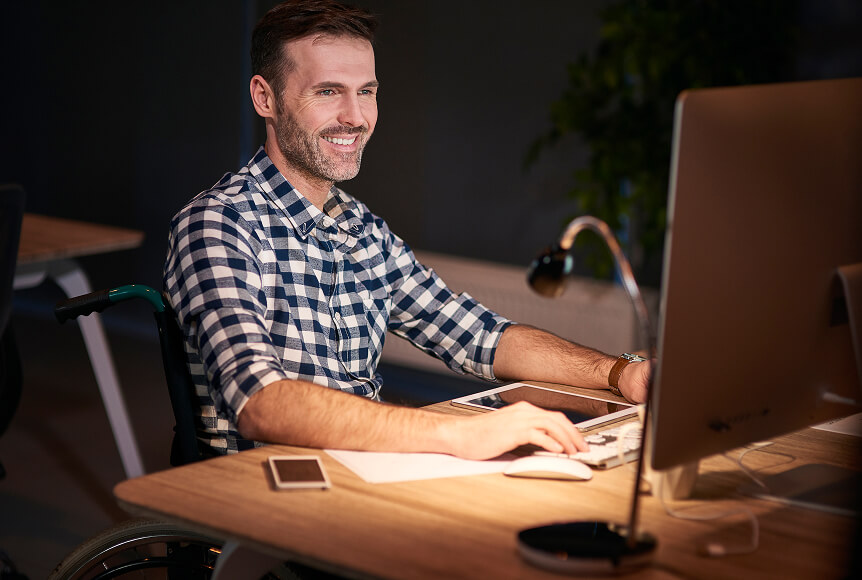 A happy man is typing on a desktop, enjoying Newshosting's top-rated Usenet service.