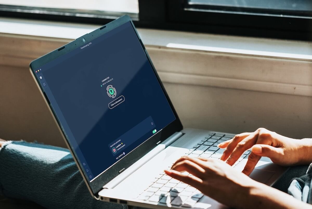 A closeup of a laptop showing the PrivadoVPN logo and two hands typing on it.